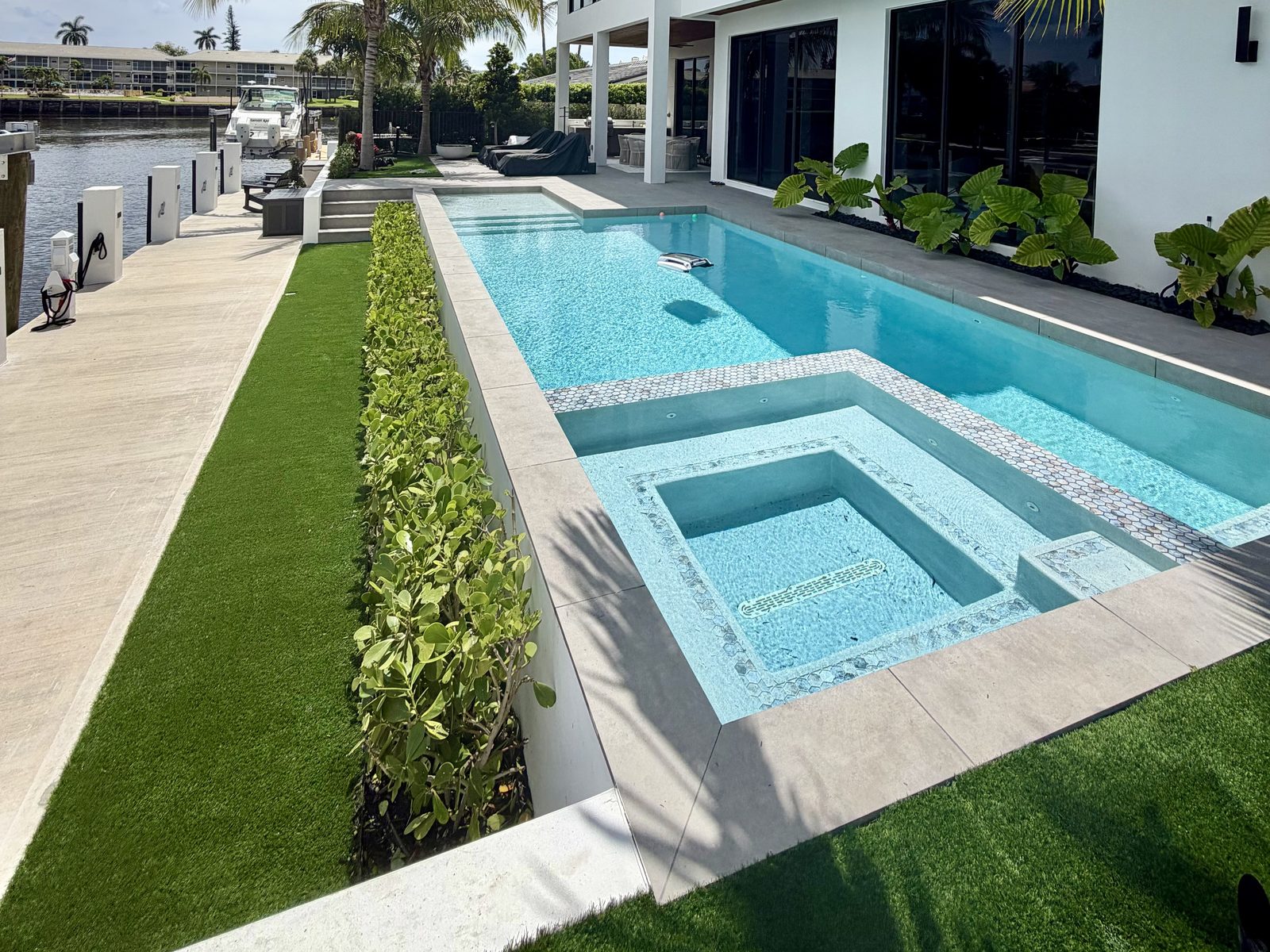 Waterfront pool landscape with turf, hedge and palms